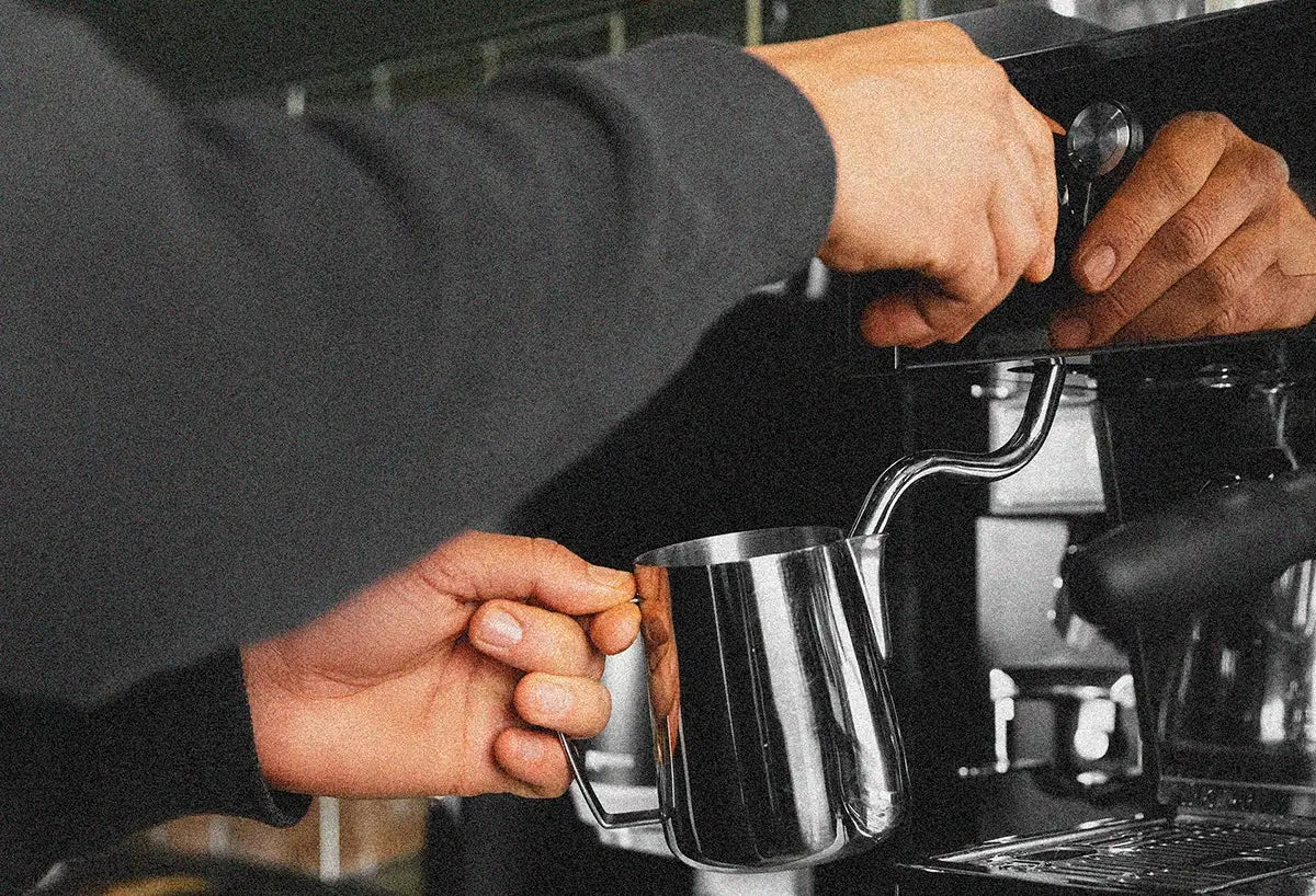 Person using a milk frother on an espresso machine - Browse restaurant equipment maintenance plans from Better Brands
